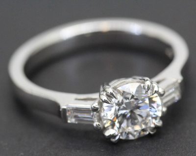 Elegant diamond engagement ring with a central round cut stone and baguette side stones.