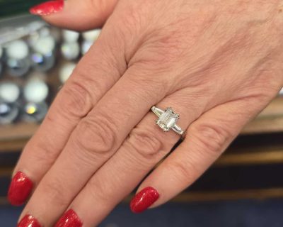 Stunning emerald cut diamond engagement ring on a woman's hand with red nails.