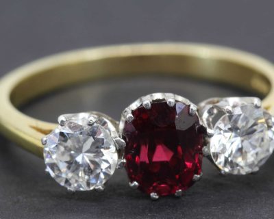 Gold ring with central ruby and two side diamonds, fine jewelry piece.