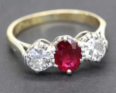 Ruby and diamond engagement ring with a central oval ruby flanked by two diamonds.