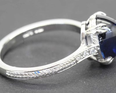 Silver ring featuring a large, deep blue gemstone and intricate engraved band design.