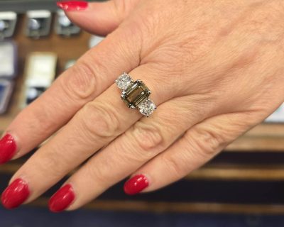 Emerald cut diamond ring with side stones on a woman's finger, showcasing fine jewelry craftsmanship.