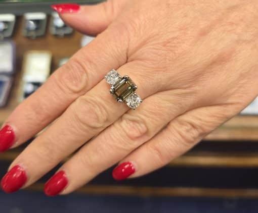 Emerald cut diamond ring with side stones on a woman's finger, showcasing fine jewelry craftsmanship.