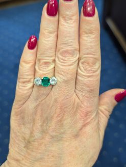 Main photo of Colombian emerald and diamond three stone ring on a hand