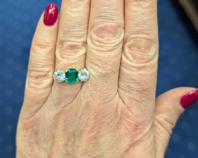 Main photo of Colombian emerald and diamond three stone ring on a hand