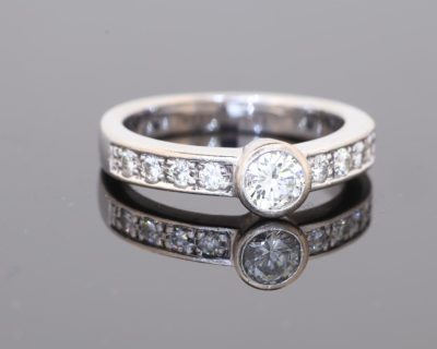 Elegant and contemporary in style, this diamond ring combines the clean lines of a bezel setting with the enduring brilliance of diamonds. Its refined design balances the prominence of the central stone with the delicate sparkle of diamond-set shoulders, creating a sophisticated addition to a fine jewellery collection.