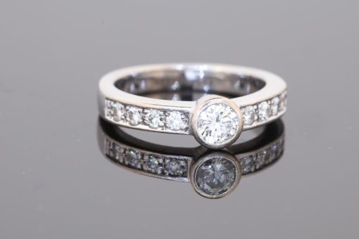 Elegant and contemporary in style, this diamond ring combines the clean lines of a bezel setting with the enduring brilliance of diamonds. Its refined design balances the prominence of the central stone with the delicate sparkle of diamond-set shoulders, creating a sophisticated addition to a fine jewellery collection.