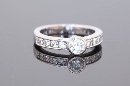 Elegant and contemporary in style, this diamond ring combines the clean lines of a bezel setting with the enduring brilliance of diamonds. Its refined design balances the prominence of the central stone with the delicate sparkle of diamond-set shoulders, creating a sophisticated addition to a fine jewellery collection.