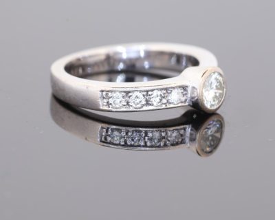 Elegant and contemporary in style, this diamond ring combines the clean lines of a bezel setting with the enduring brilliance of diamonds. Its refined design balances the prominence of the central stone with the delicate sparkle of diamond-set shoulders, creating a sophisticated addition to a fine jewellery collection.