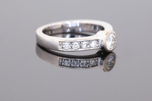 Elegant and contemporary in style, this diamond ring combines the clean lines of a bezel setting with the enduring brilliance of diamonds. Its refined design balances the prominence of the central stone with the delicate sparkle of diamond-set shoulders, creating a sophisticated addition to a fine jewellery collection.