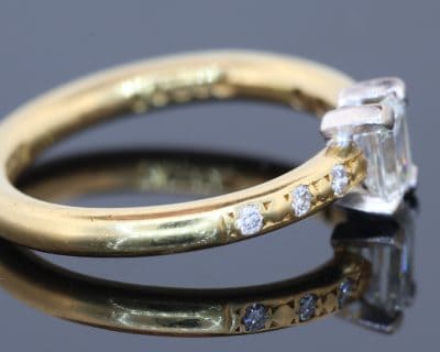 An elegant diamond engagement ring combining the timeless appeal of an emerald-cut diamond with the understated sophistication of 18kt gold. Its clean lines and subtle diamond detailing create a refined design that balances classic elegance with contemporary simplicity.