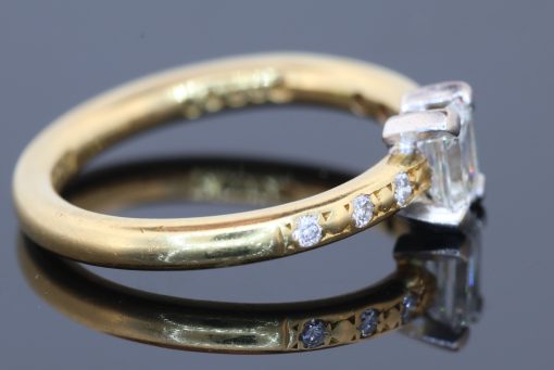 An elegant diamond engagement ring combining the timeless appeal of an emerald-cut diamond with the understated sophistication of 18kt gold. Its clean lines and subtle diamond detailing create a refined design that balances classic elegance with contemporary simplicity.