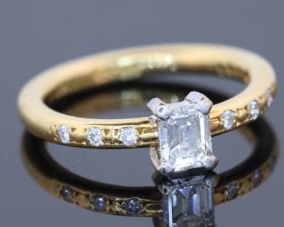 An elegant diamond engagement ring combining the timeless appeal of an emerald-cut diamond with the understated sophistication of 18kt gold. Its clean lines and subtle diamond detailing create a refined design that balances classic elegance with contemporary simplicity.