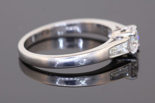 A refined diamond engagement ring combining timeless elegance with crisp geometric detailing. Set in platinum, this design pairs a classic claw-set centre diamond with baguette-cut shoulder stones, creating a sophisticated balance of brilliance and clean lines.