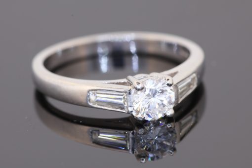A refined diamond engagement ring combining timeless elegance with crisp geometric detailing. Set in platinum, this design pairs a classic claw-set centre diamond with baguette-cut shoulder stones, creating a sophisticated balance of brilliance and clean lines.