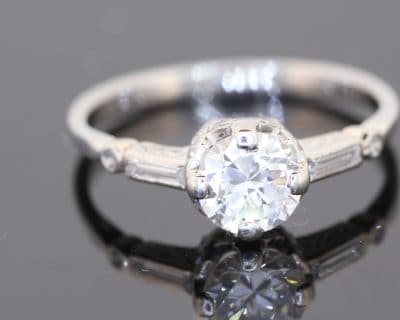 This Art Deco diamond engagement ring captures the elegance and geometric sophistication of the period. Combining a brilliant-cut centre diamond with baguette-cut shoulders and intricate engraved details, it is a distinctive jewel that celebrates the craftsmanship and design sensibility associated with Art Deco jewellery.