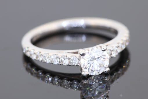 A timeless diamond engagement ring, combining the brilliance of a round brilliant-cut centre diamond with the refined sparkle of diamond-set shoulders. Crafted in 18kt white gold, this elegant design offers a sophisticated expression of enduring commitment.