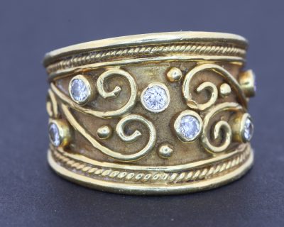 A striking wide gold ring that combines the warmth of precious metal with the brilliance of diamonds and the intricate beauty of applied filigree. Its decorative detailing gives the piece a distinctive character, balancing the bold presence of a broad band with the refinement of traditional goldsmithing.