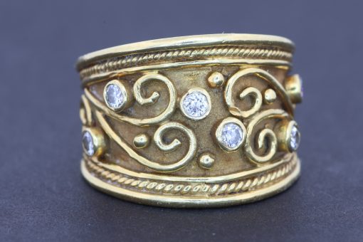A striking wide gold ring that combines the warmth of precious metal with the brilliance of diamonds and the intricate beauty of applied filigree. Its decorative detailing gives the piece a distinctive character, balancing the bold presence of a broad band with the refinement of traditional goldsmithing.