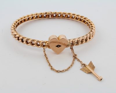 A rare antique 15-karat gold bangle, distinguished by its romantic heart lock and Cupid’s arrow key. Combining symbolic motifs of love and devotion with the enduring appeal of antique gold jewellery, this charming piece offers a glimpse into the sentimental traditions of earlier jewellery design.
