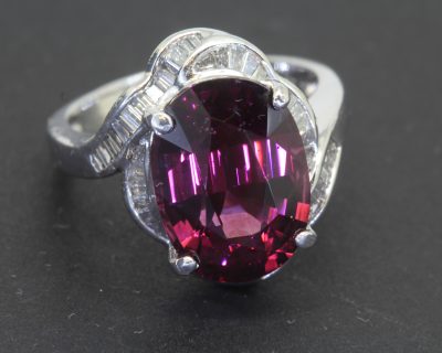 A striking Art Deco ring, combining the bold glamour of the period with an imaginative arrangement of gemstones. Celebrated for its geometric precision and distinctive decorative motifs, Art Deco jewellery often balances strong design with intricate detailing. This ring offers a particularly captivating interpretation, pairing a substantial 9-carat garnet with the refined sparkle of baguette-cut diamonds.