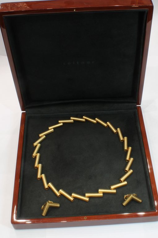 A striking 18-carat yellow-gold necklace by Manfred Seitner of Vienna, distinguished by its sculptural geometry and beautifully restrained use of texture. The necklace has a distinctly architectural quality, combining articulated cylindrical forms with subtle variations in angle to create a dynamic and highly contemporary silhouette. The accompanying matching ear clips complete the suite, echoing the necklace's geometric language in a beautifully cohesive design.