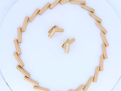 A striking 18-carat yellow-gold necklace by Manfred Seitner of Vienna, distinguished by its sculptural geometry and beautifully restrained use of texture. The necklace has a distinctly architectural quality, combining articulated cylindrical forms with subtle variations in angle to create a dynamic and highly contemporary silhouette. The accompanying matching ear clips complete the suite, echoing the necklace's geometric language in a beautifully cohesive design.