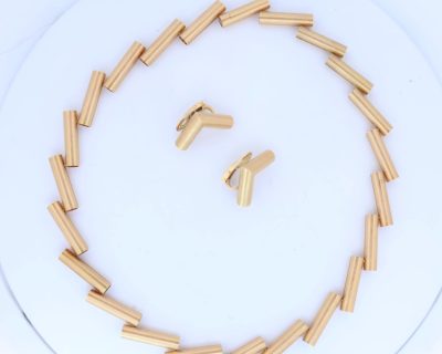 A striking 18-carat yellow-gold necklace by Manfred Seitner of Vienna, distinguished by its sculptural geometry and beautifully restrained use of texture. The necklace has a distinctly architectural quality, combining articulated cylindrical forms with subtle variations in angle to create a dynamic and highly contemporary silhouette. The accompanying matching ear clips complete the suite, echoing the necklace's geometric language in a beautifully cohesive design.