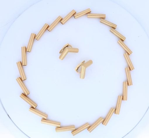 A striking 18-carat yellow-gold necklace by Manfred Seitner of Vienna, distinguished by its sculptural geometry and beautifully restrained use of texture. The necklace has a distinctly architectural quality, combining articulated cylindrical forms with subtle variations in angle to create a dynamic and highly contemporary silhouette. The accompanying matching ear clips complete the suite, echoing the necklace's geometric language in a beautifully cohesive design.
