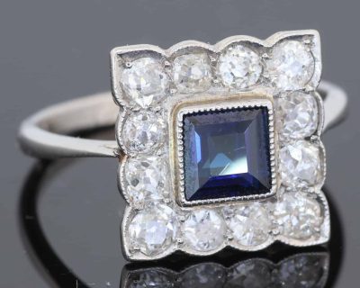A charming antique sapphire and diamond cluster ring, dating to circa 1923, set in platinum and carrying a wonderfully personal inscription inside the shank: “FHB to Gwen 1923”. The dated dedication gives this elegant jewel a tangible connection to its original owners, transforming it from a beautiful piece of jewellery into a small piece of personal history. The inscription suggests that the ring was presented to Gwen in 1923, making it particularly evocative as a period gift.