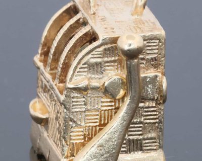 A wonderfully whimsical gold novelty charm in the form of a one-armed bandit, capturing the playful spirit of traditional gambling machines in miniature. The charm is particularly appealing for its working mechanism, transforming an instantly recognisable slot machine into an ingenious piece of novelty jewellery.