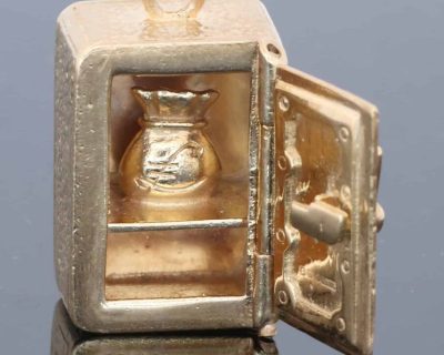 A charming and unusual gold novelty safe charm, designed as a miniature representation of a traditional safe and incorporating a delightful hidden surprise. Novelty charms of this kind transformed familiar objects into miniature works of jewellery, often with an element of humour or concealed detail. This example is particularly appealing for its clever association between a safe and its precious contents.
