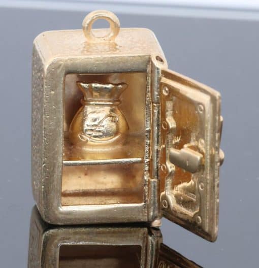 A charming and unusual gold novelty safe charm, designed as a miniature representation of a traditional safe and incorporating a delightful hidden surprise. Novelty charms of this kind transformed familiar objects into miniature works of jewellery, often with an element of humour or concealed detail. This example is particularly appealing for its clever association between a safe and its precious contents.