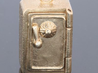 A charming and unusual gold novelty safe charm, designed as a miniature representation of a traditional safe and incorporating a delightful hidden surprise. Novelty charms of this kind transformed familiar objects into miniature works of jewellery, often with an element of humour or concealed detail. This example is particularly appealing for its clever association between a safe and its precious contents.