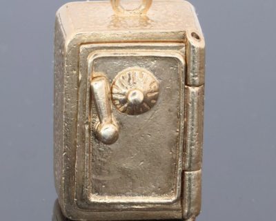 A charming and unusual gold novelty safe charm, designed as a miniature representation of a traditional safe and incorporating a delightful hidden surprise. Novelty charms of this kind transformed familiar objects into miniature works of jewellery, often with an element of humour or concealed detail. This example is particularly appealing for its clever association between a safe and its precious contents.