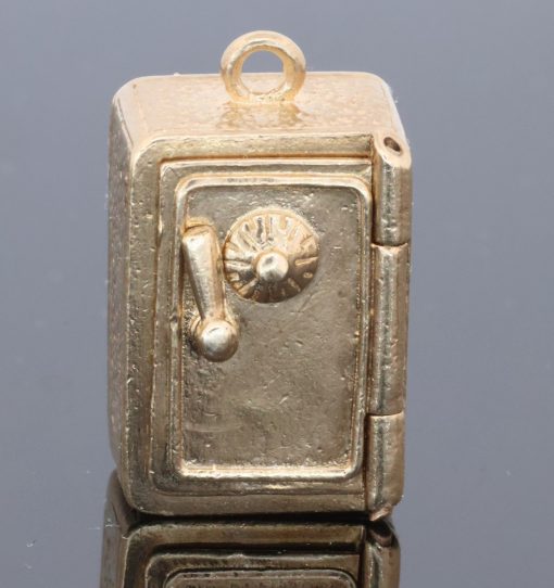 A charming and unusual gold novelty safe charm, designed as a miniature representation of a traditional safe and incorporating a delightful hidden surprise. Novelty charms of this kind transformed familiar objects into miniature works of jewellery, often with an element of humour or concealed detail. This example is particularly appealing for its clever association between a safe and its precious contents.